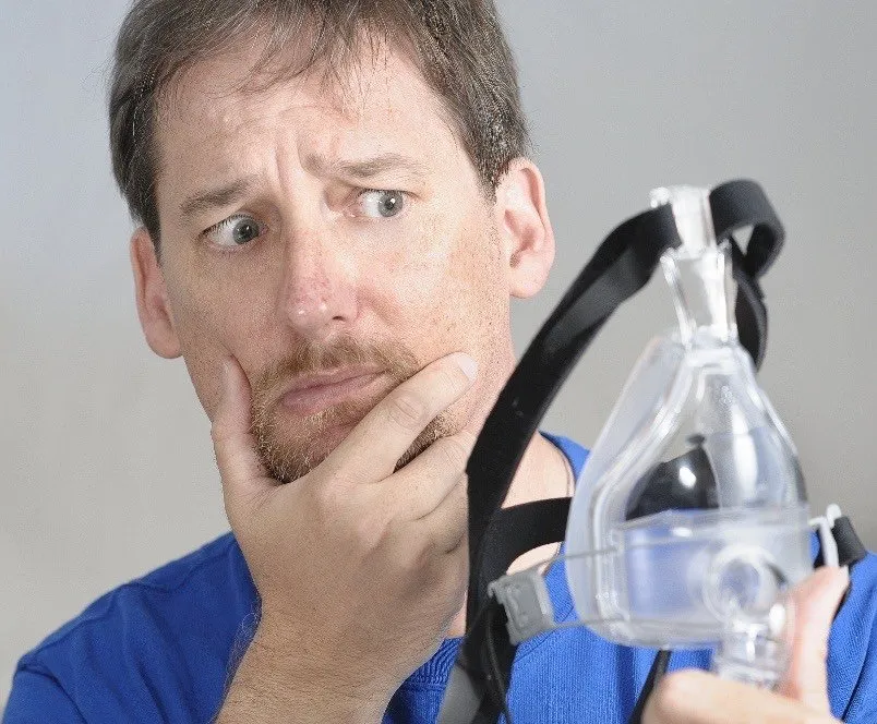 A frustrated man holding a CPAP mask